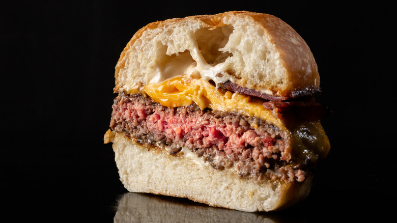 A medium-rare burger cut in half, on a black backdrop.