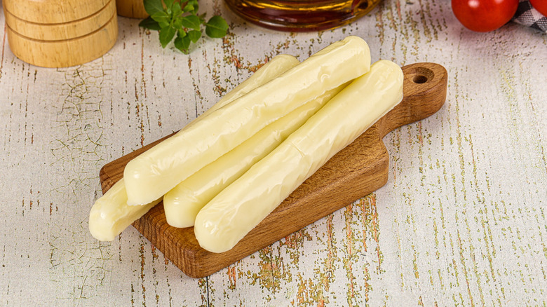 Sticks of mozzarella cheese are stacked on a cutting board.