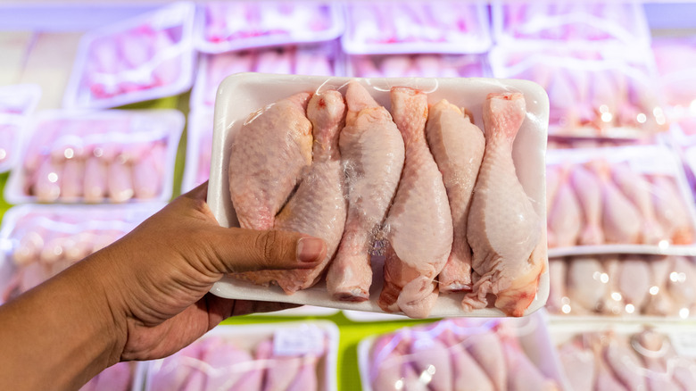 Hand holding a package of chicken drumsticks