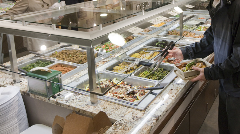 Person filling a box at Whole Foods' hot food bar with vegetables, grains, and proteins