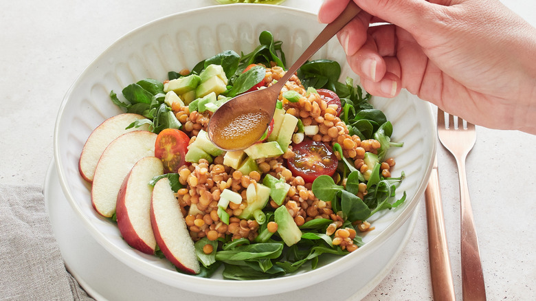 Person spooning salad dressing on salad with apples, spinach, and avocado