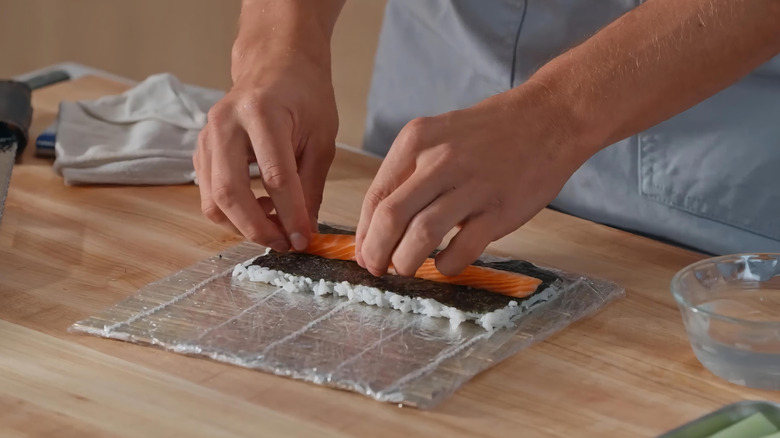 hands making a salmon, nori, and rice sushi roll