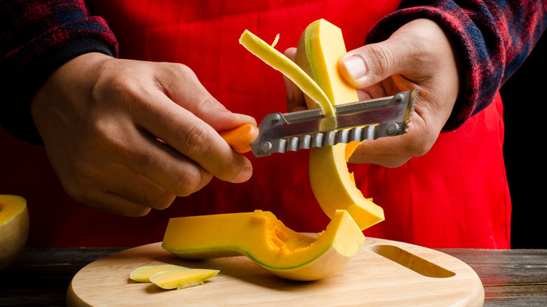 A cook peeling the skin of a butternut squash.