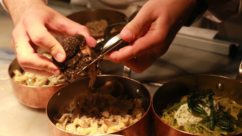 A person's hands shave truffles over pasta.