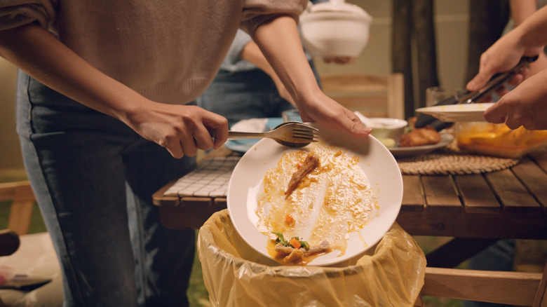 A person scraping a dirty dish into a bin