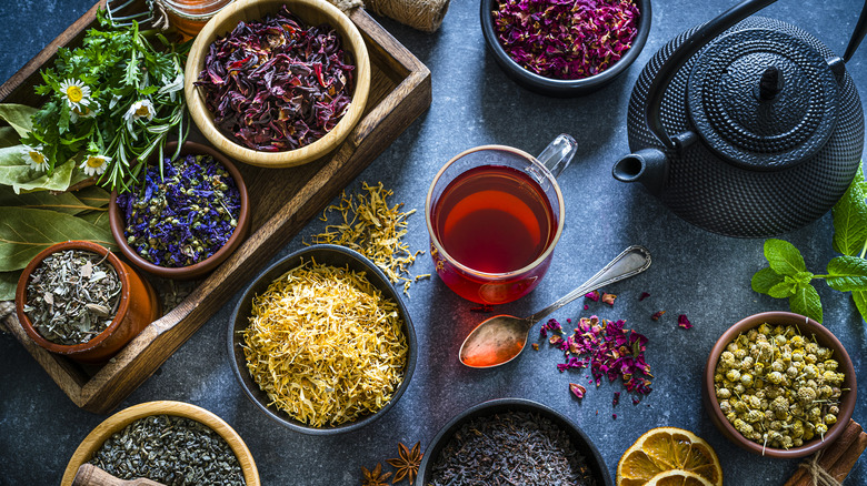Dried tea in bowls surround a glass mug of tea and teapot