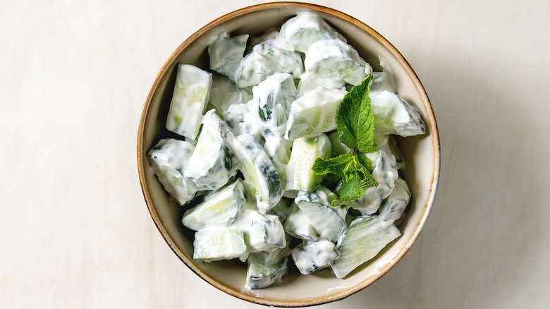 A bowl of cucumber salad with yoghurt on a cream colored background
