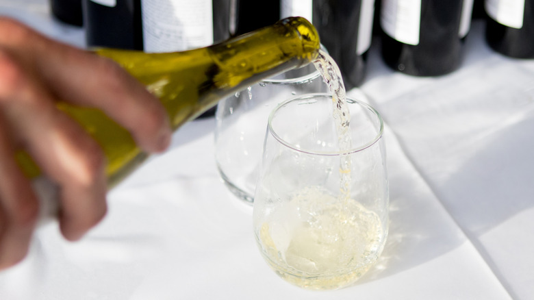 Person pouring white wine from a bottle into a stemless wine glass