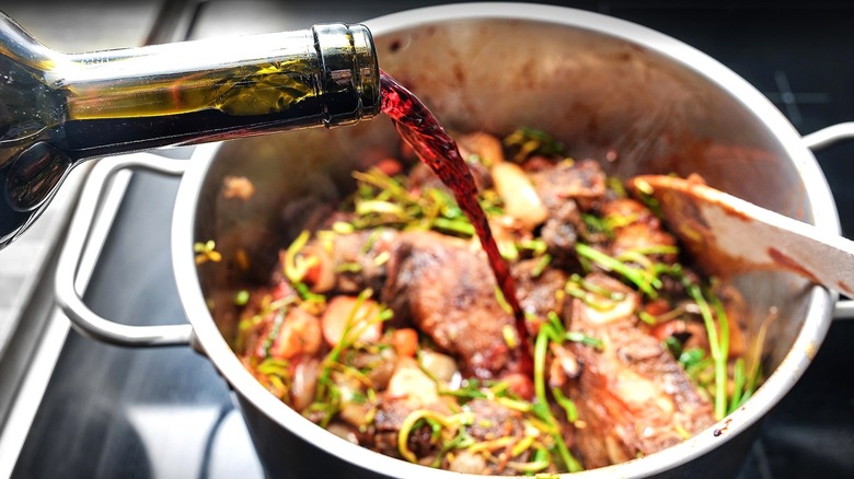 Red wine being poured into a pot filled with meat and greens.