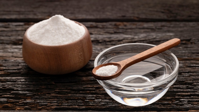A small wooden bowl of baking soda beside a small glass bowl of water and a spoon full of baking soda