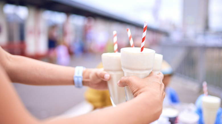 A person's hands are seen carryong three milkshakes with straws.