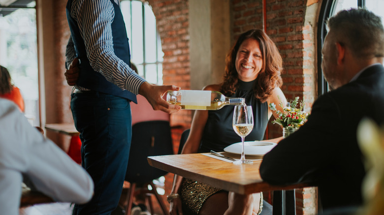 Waiter pouring a glass of wine for a couple eating at a French restaurant