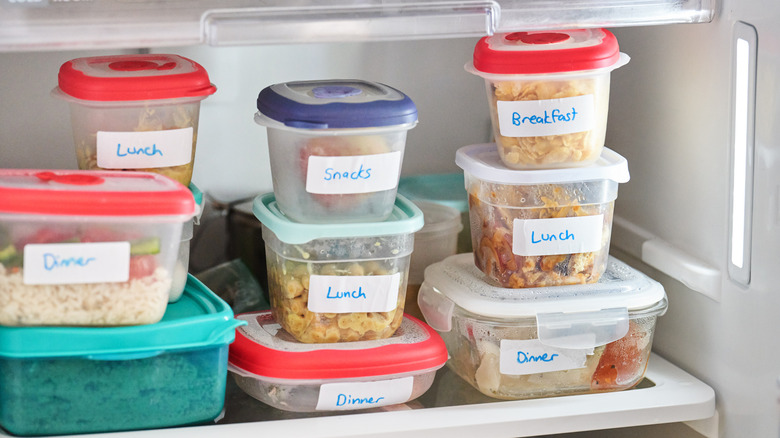 Multiple labeled plastic food containers in fridge.
