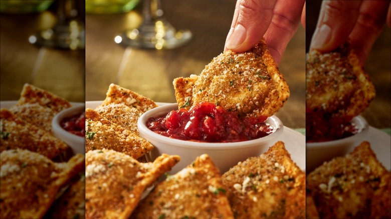 Hand dipping Olive Garden's toasted ravioli into tomato sauce