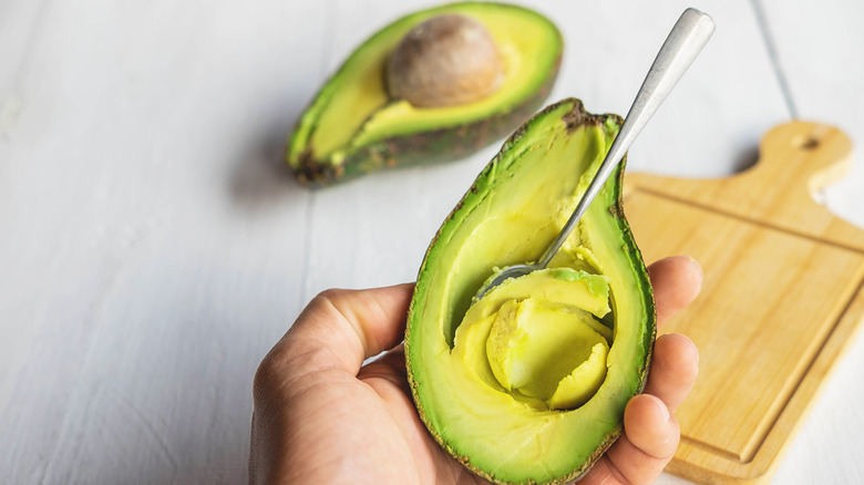 Hand holding avocado with silver spoon