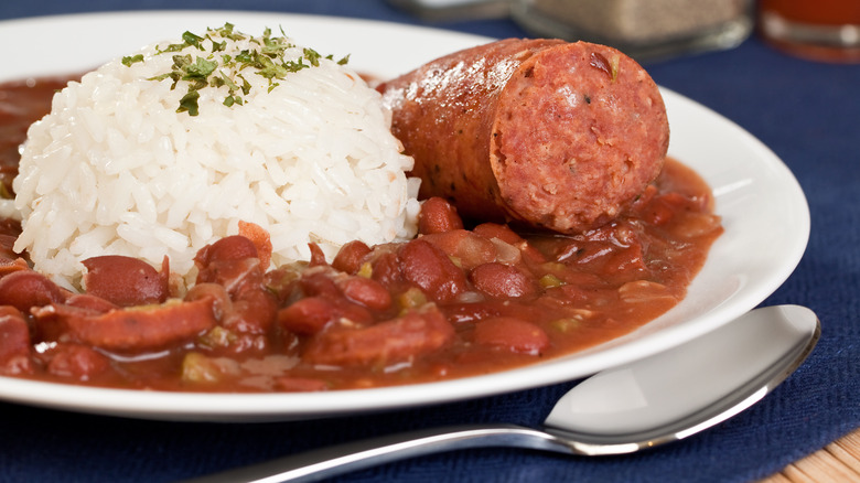 A bowl of red beans and rice with a sausage on it.