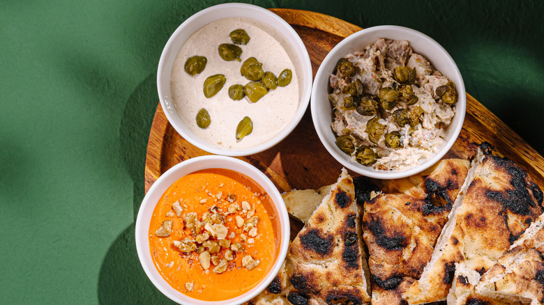 A wooden platter loaded with various dips and naan bread