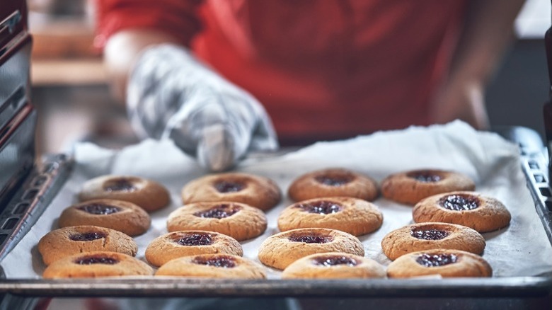 Gloved hand removing aluminum baking pan of cookies from the oven