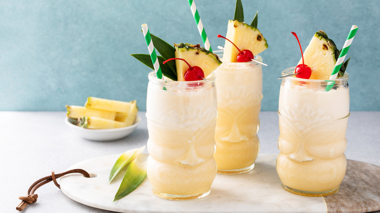 Three piña colada cocktails with cherry and pineapple garnish