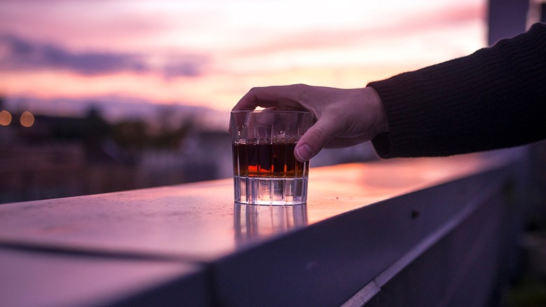 Person holding a neat glass of whiskey on a rooftop