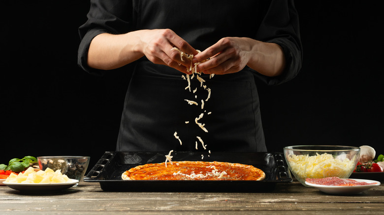A chef sprinkles cheese on an unbaked pizza.