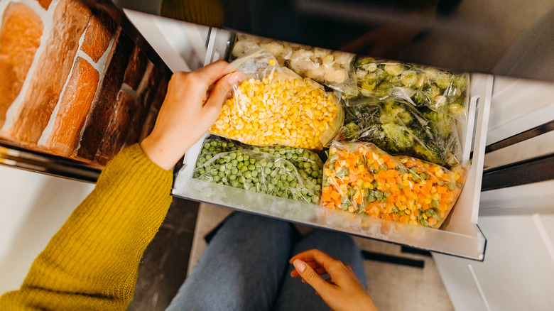 Hand reaching into a freezer full of vegetables.