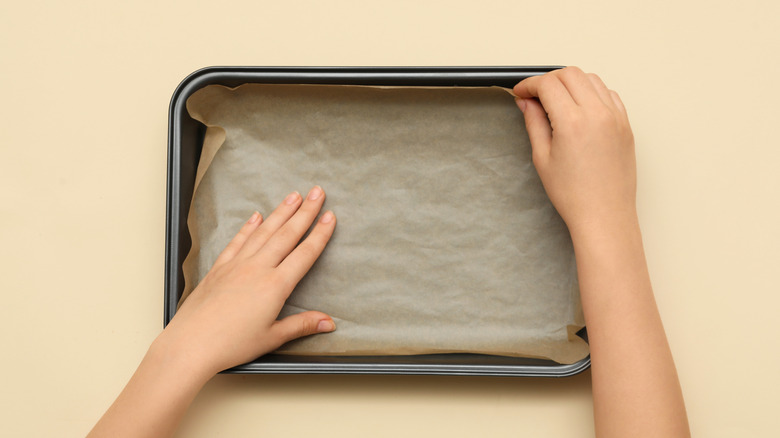 Person lining a baking pan with parchment paper