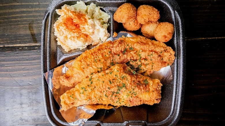 Takeout box with potato salad, fried fish, and hush puppies