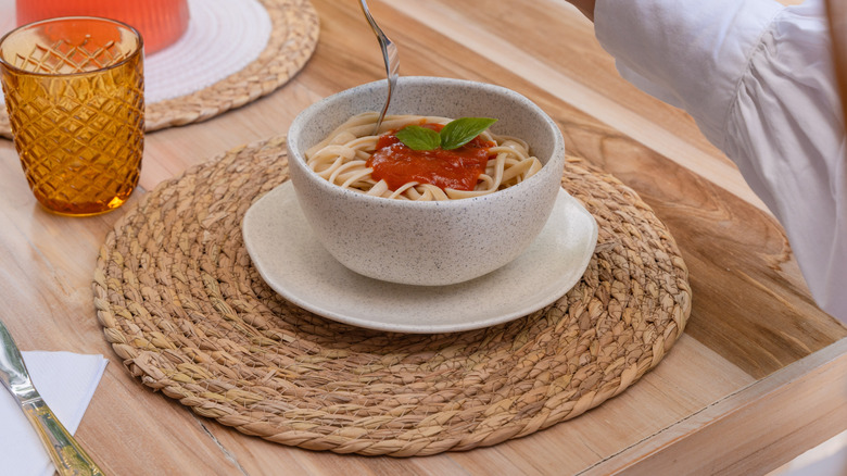 A round, rattan placemat with a bowl of noodles.