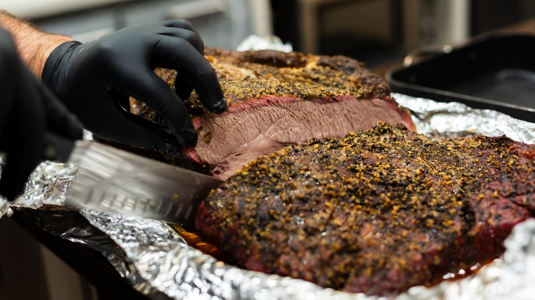 A person's hands are seen slicing brisket with a large knife.
