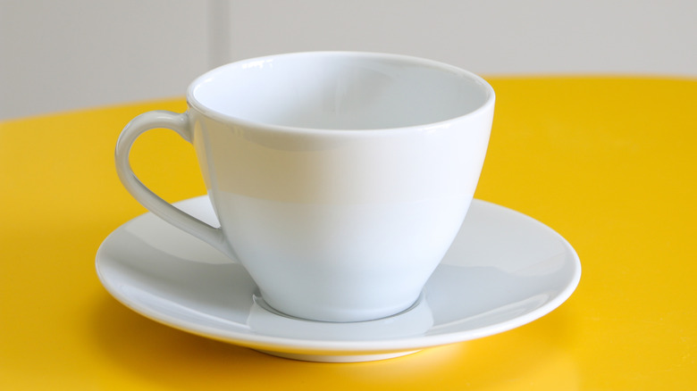A clean white coffee cup on a saucer atop a bright yellow table.