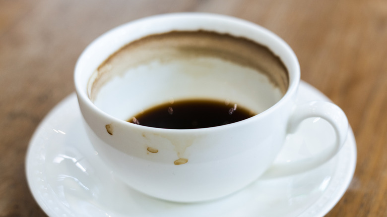 A dainty white coffee cup on a saucer is stained inside with a coffee ring.