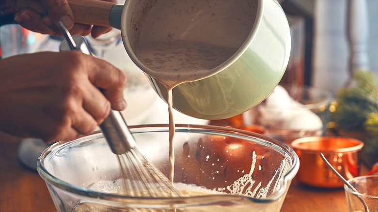 Person holding a saucepan and whisk while tempering eggs with hot milk