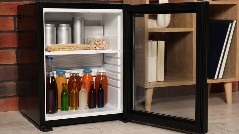 A mini fridge stacked with drinks, snacks, and containers