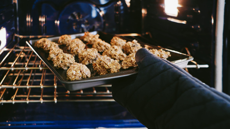 Oven mitt hand adding oatmeal cookies to oven