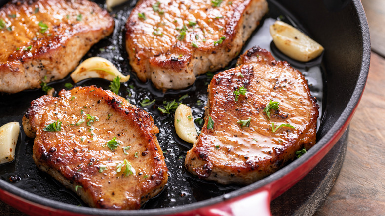 Golden sauteed pork chops in a pan with garlic and herbs