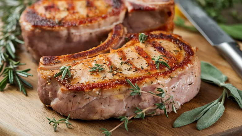 Pork chops with fresh herbs rest on a cutting board.