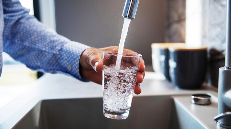 A man filling a glass from a kitchen tap