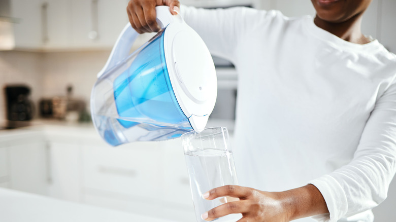 A woman pouring a glass of water from a filtered water pitcher