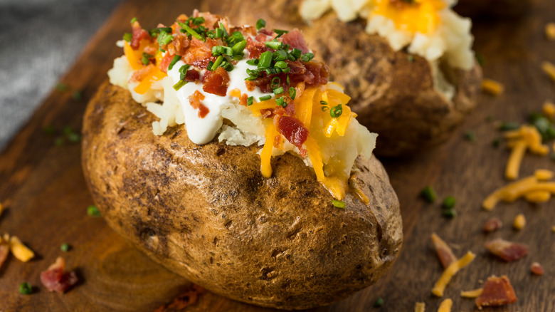 A baked potato is dressed with sour cream, cheese, bacon, and chives