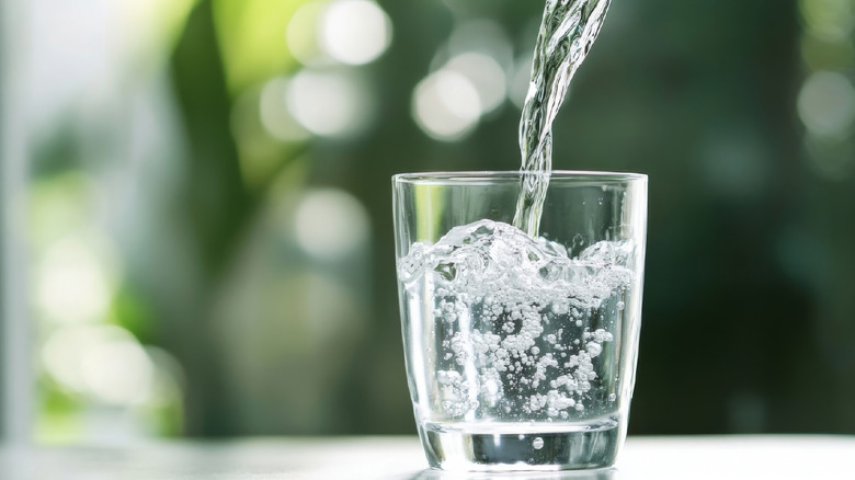 Pouring Water into a Glass Against a Green Blurred Background