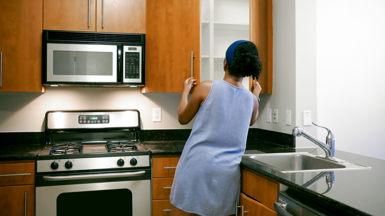 Person touring the kitchen of an empty apartment, opening a cabinet