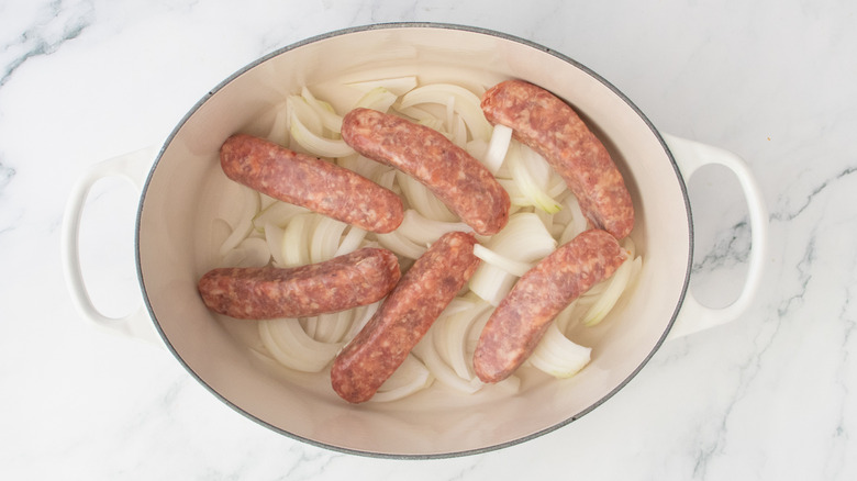 Raw brats and onions in a large Dutch oven.