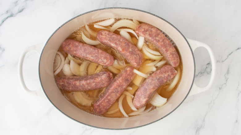 Raw brats and onions in a large Dutch oven covered in beer