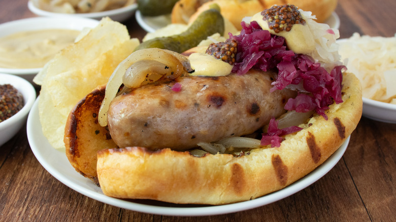 Side shot of dressed beer brats and plain beer brats on wood with condiments
