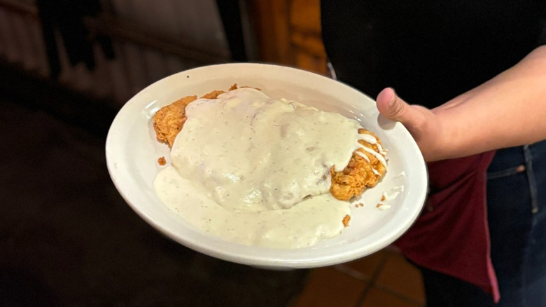 Waitress holding Texas Roadhouse's country fried chicken with cream gravy served on a white plate