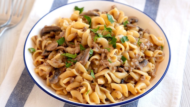 Creamy ground beef and mushroom pasta in a white, blue-rimmed bowl over a blue and white striped cloth napkin