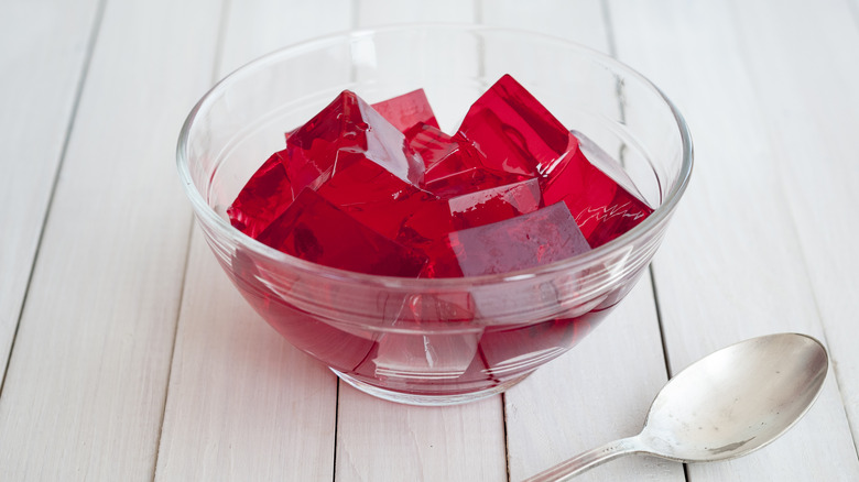 A bowl of Jell-O cubes with a spoon sitting on the side.