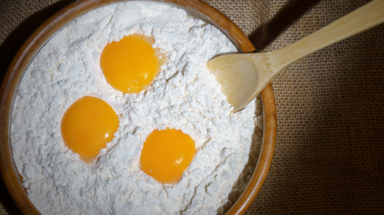 A bowl of flour with three eggs dotted on top.