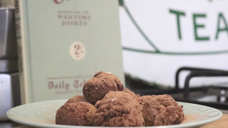 Chocolate truffles made with mashed potatoes on a plate with the recipe book in the background.